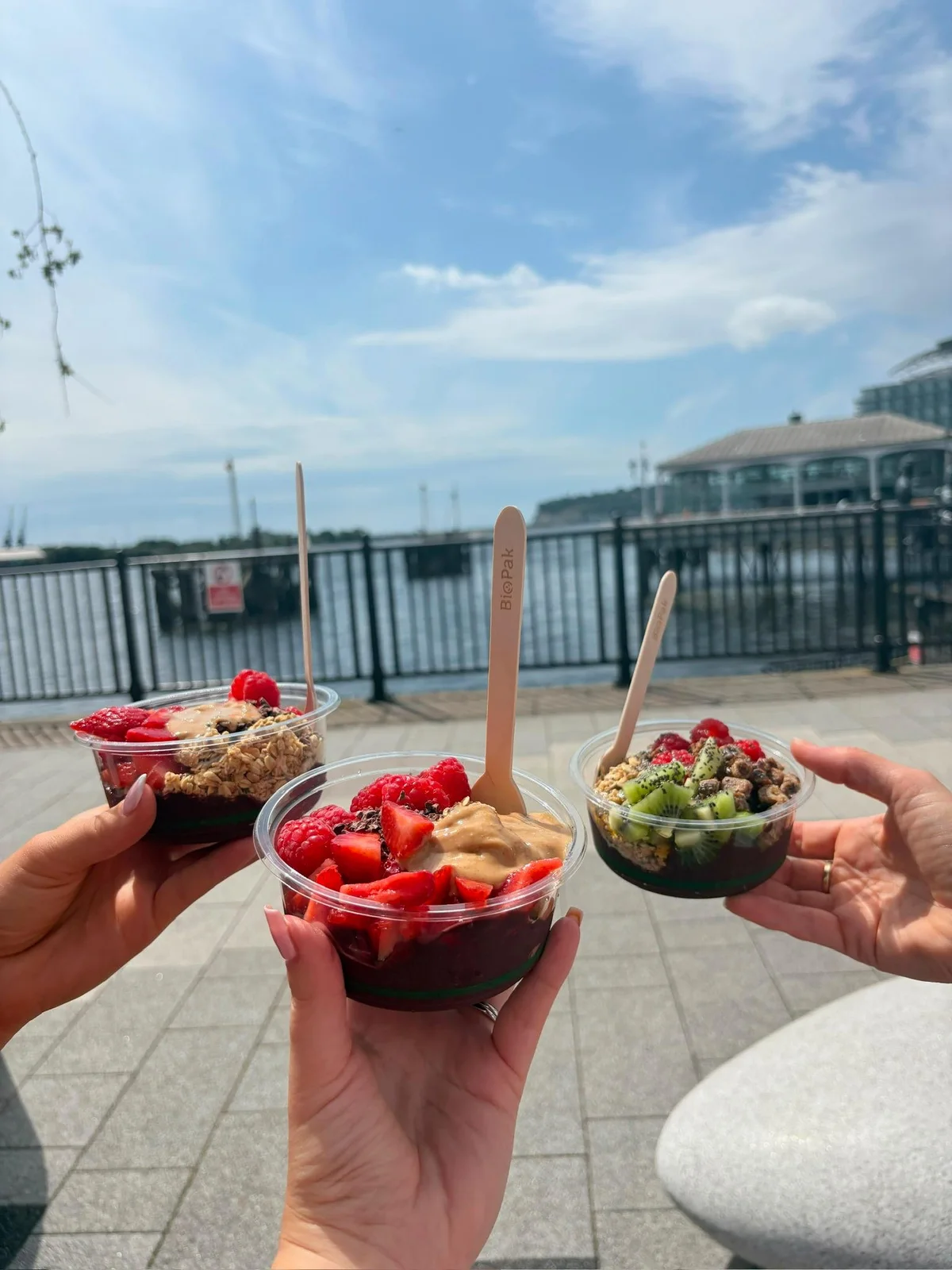 Three friends holding their açaí bowls beside Cardiff Bay