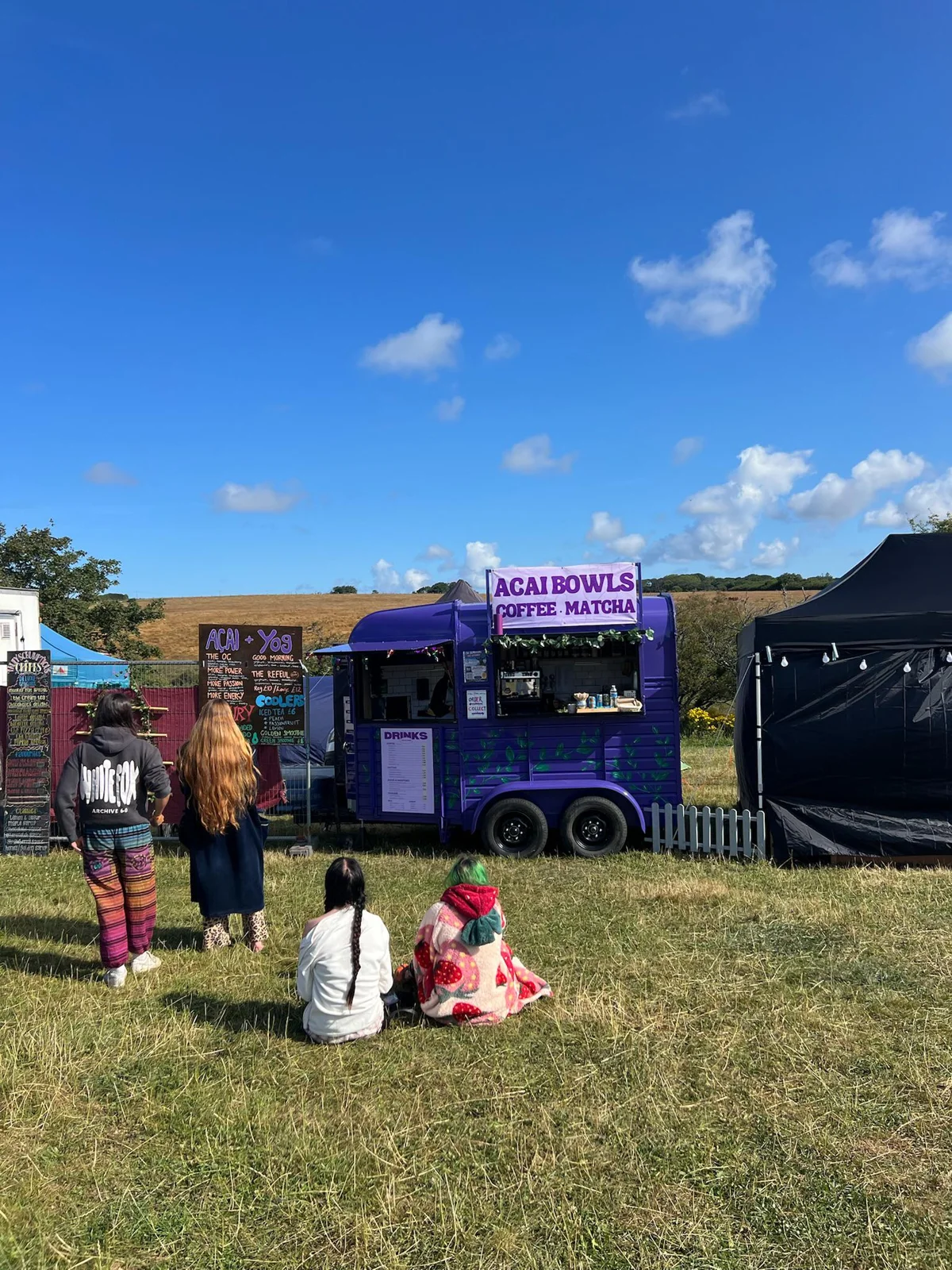 The purple horsebox at a sunny festival, with visitors enjoying the day